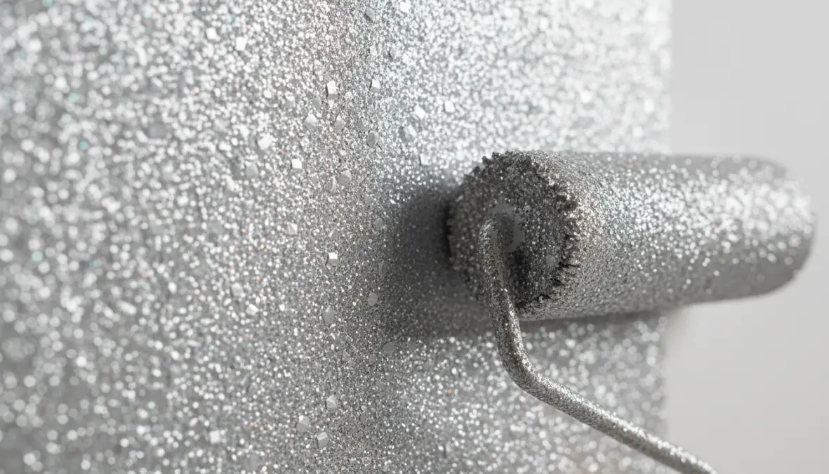 Dettaglio di parete con vernice glitter argentata e rullo per pittura che mostra l'effetto brillante